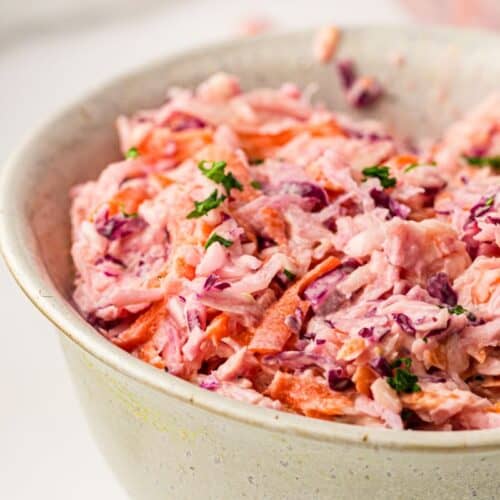 A close-up of a bowl filled with creamy coleslaw, featuring shredded cabbage, carrots, and a sprinkle of fresh herbs on top.
