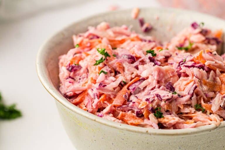 A close-up of a bowl filled with creamy coleslaw, featuring shredded cabbage, carrots, and a sprinkle of fresh herbs on top.