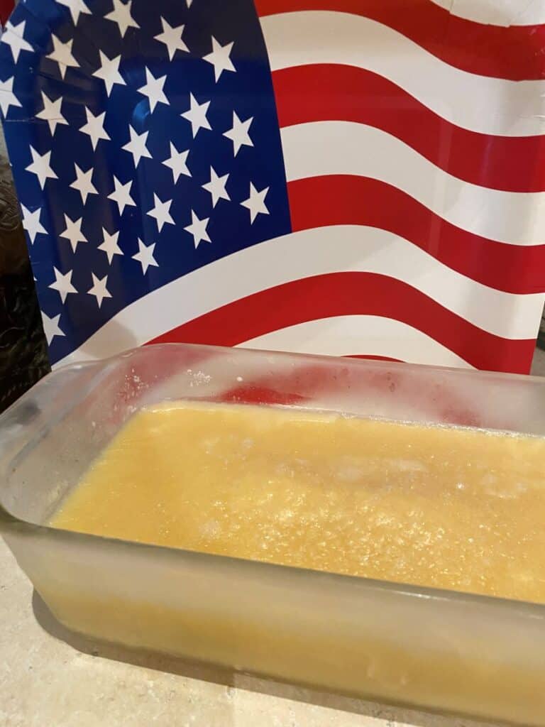 A glass dish filled with a yellowish mixture sits on a countertop, with a large American flag decoration displayed in the background.