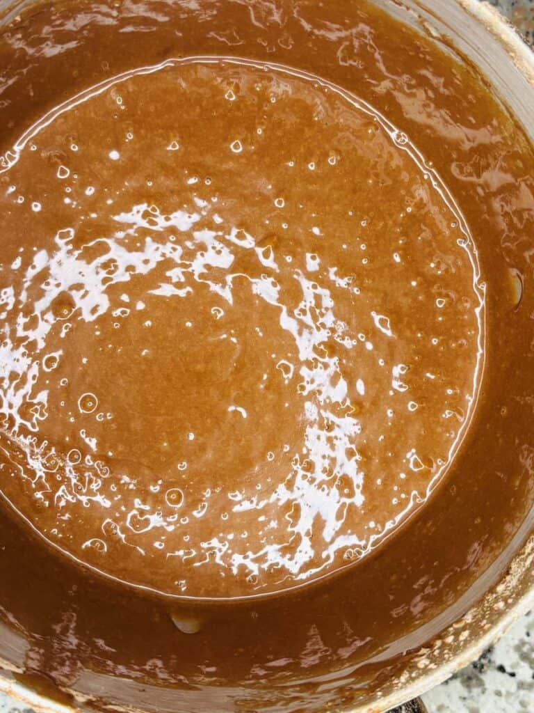 A close-up of a bowl filled with smooth, glossy chocolate cake batter, showing bubbles and swirls on the surface.