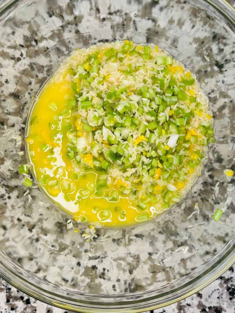 Chopped green onions and yellow egg mixture in a clear glass bowl, sitting on a speckled countertop.