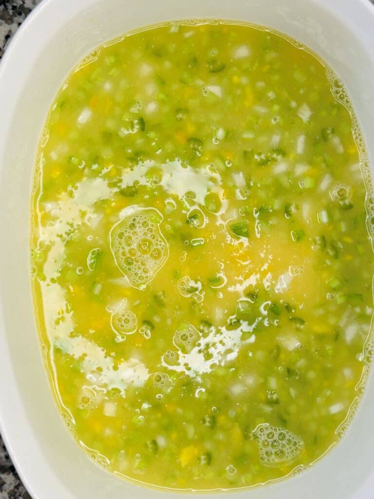 A white bowl filled with a mixture of beaten eggs, chopped onions, and green peppers; bubbles and chunks are visible on the surface.