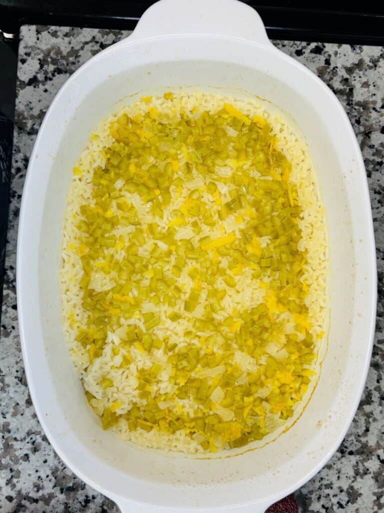 A white baking dish filled with cooked rice topped with finely chopped greenish-yellow vegetables, possibly leeks or onions, sitting on a granite countertop.