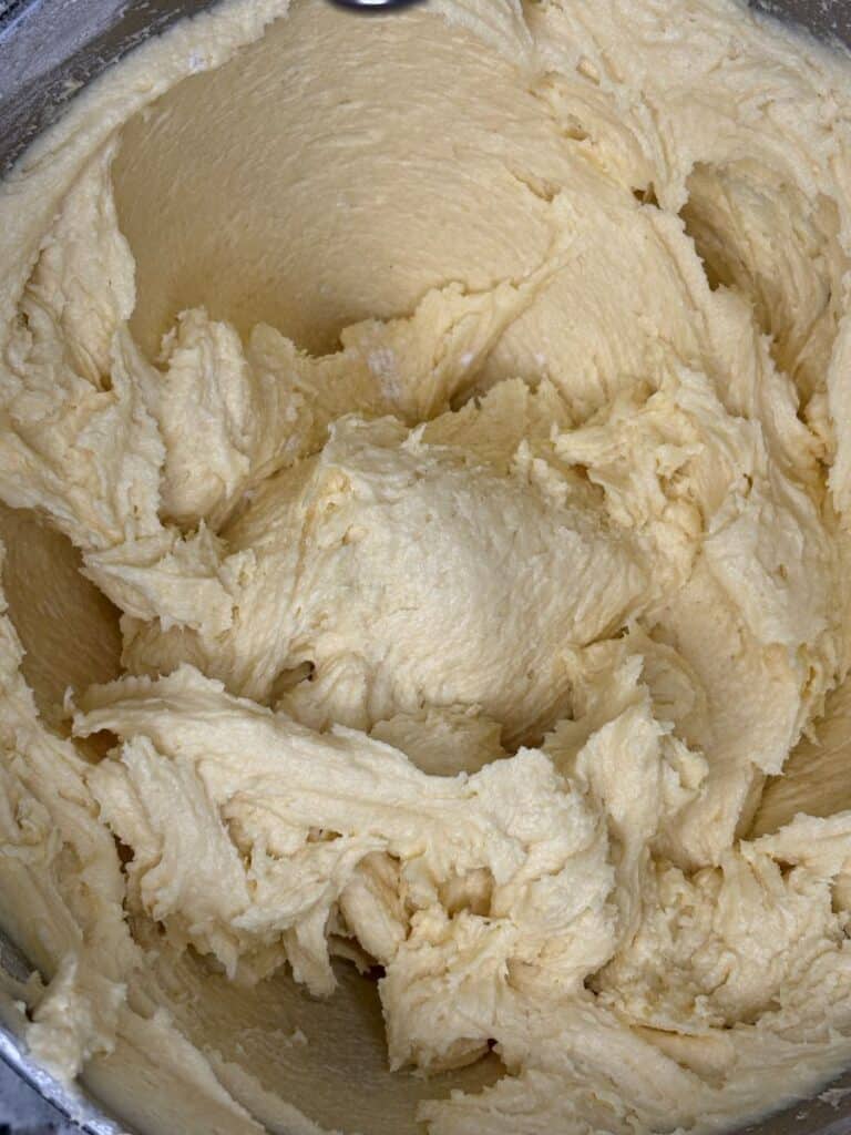 A close-up of thick, creamy, pale yellow cake batter or cookie dough in a mixing bowl, with visible swirls and peaks from mixing.