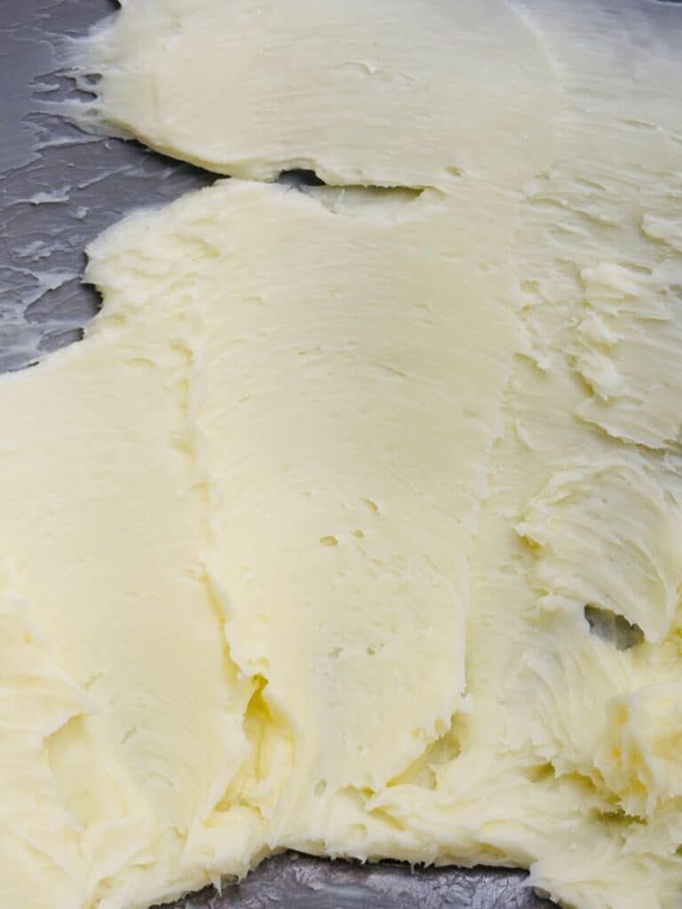 Close-up of a smooth, creamy spread of pale yellow butter on a metallic surface, showing texture and soft swirls.