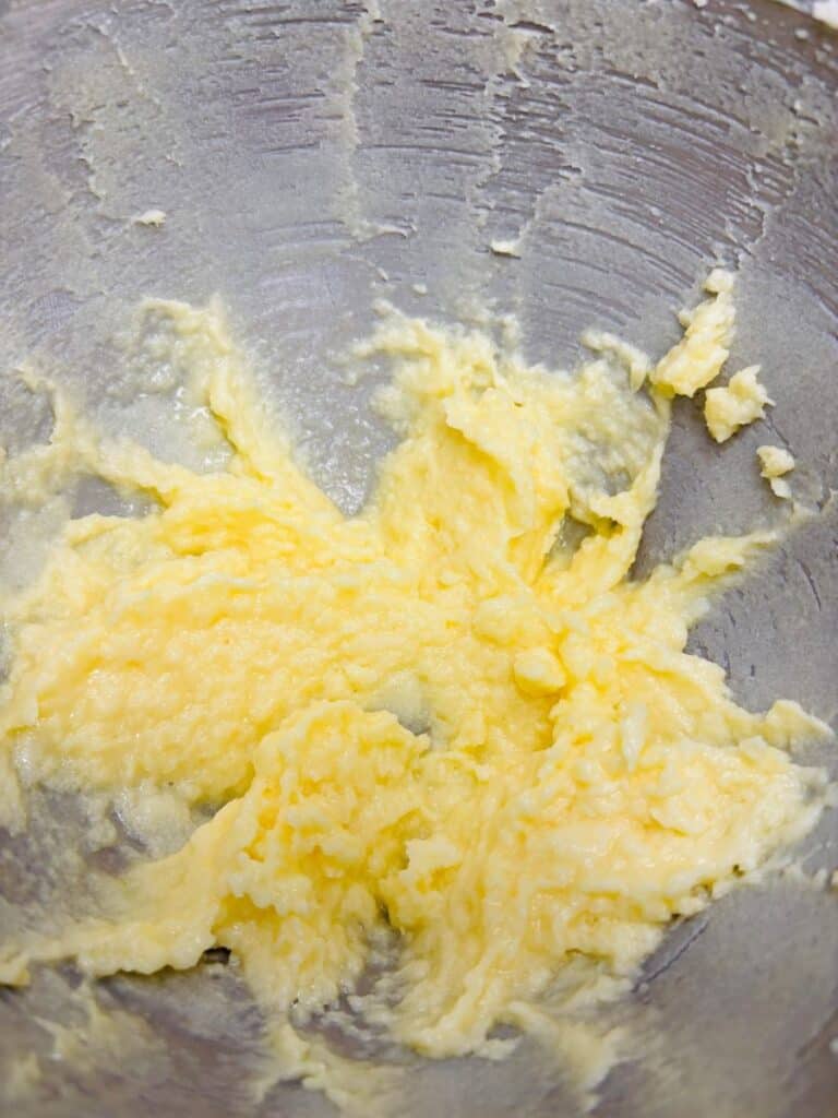 Creamed butter and sugar mixture in a metal mixing bowl, showing a light yellow, fluffy texture, commonly prepared as a base for baking cakes or cookies.