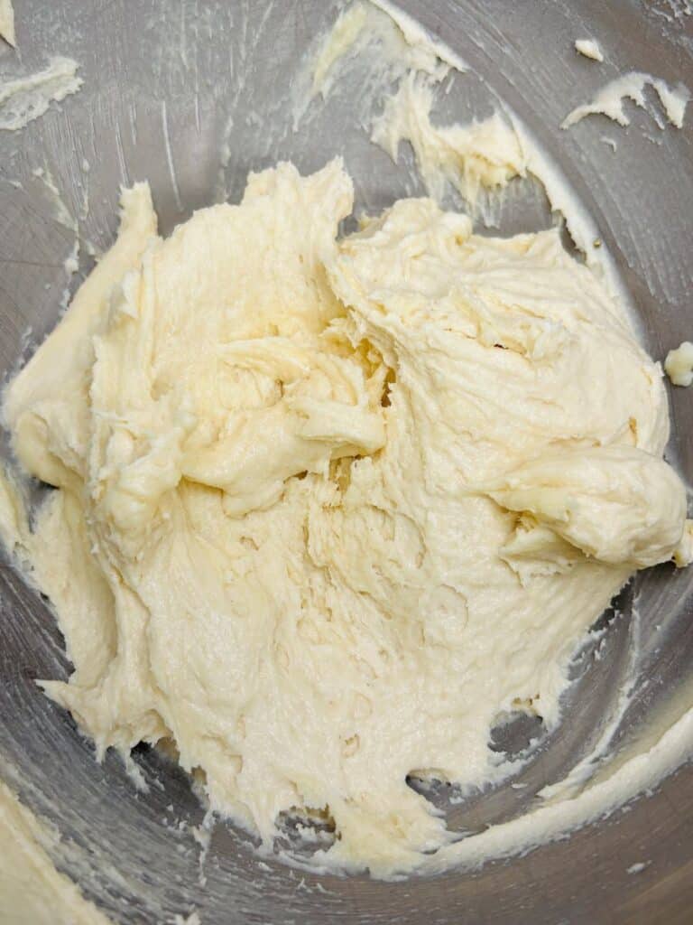 Thick, creamy, pale dough or batter is spread inside a metal mixing bowl, with visible streaks and texture from mixing.