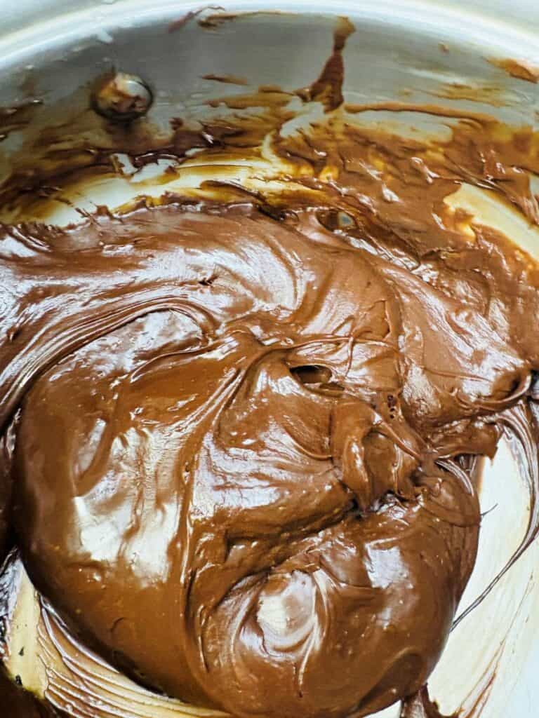 Thick, creamy melted chocolate spread swirled in a metal mixing bowl, with glossy texture and rich brown color.
