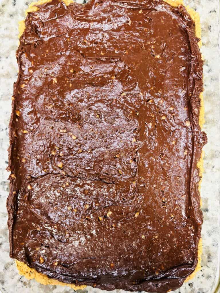 A rectangular dessert bar with a chocolate layer spread unevenly on top of a light, crumbly base, viewed from above.