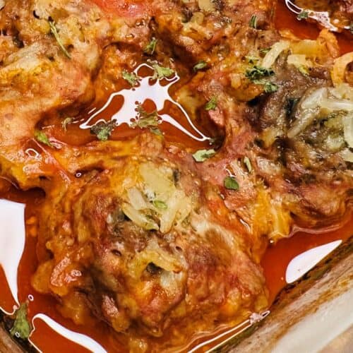 Baked stuffed cabbage rolls topped with onions and herbs in a red tomato sauce, served in a glass baking dish.
