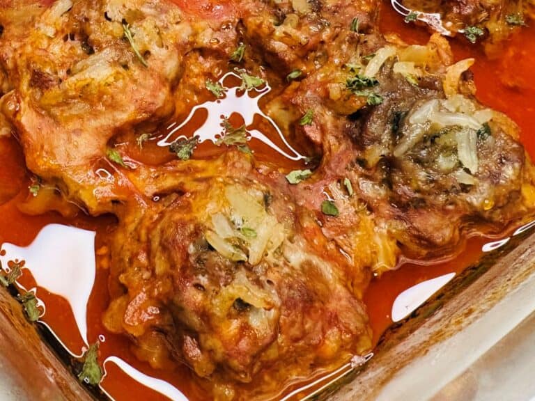 Baked stuffed cabbage rolls topped with onions and herbs in a red tomato sauce, served in a glass baking dish.
