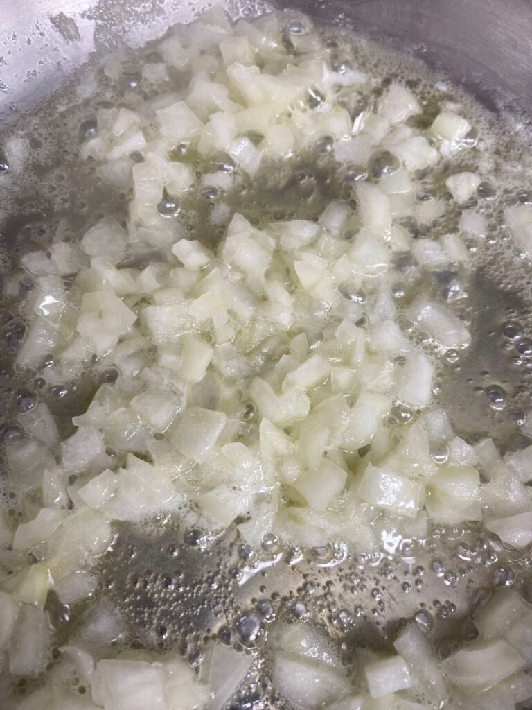 Diced onions sizzling and softening in a pan with bubbling oil or butter.