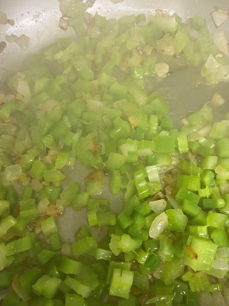 Diced celery and onions sautéing in a pan, with some pieces lightly browned and steam rising from the mixture.