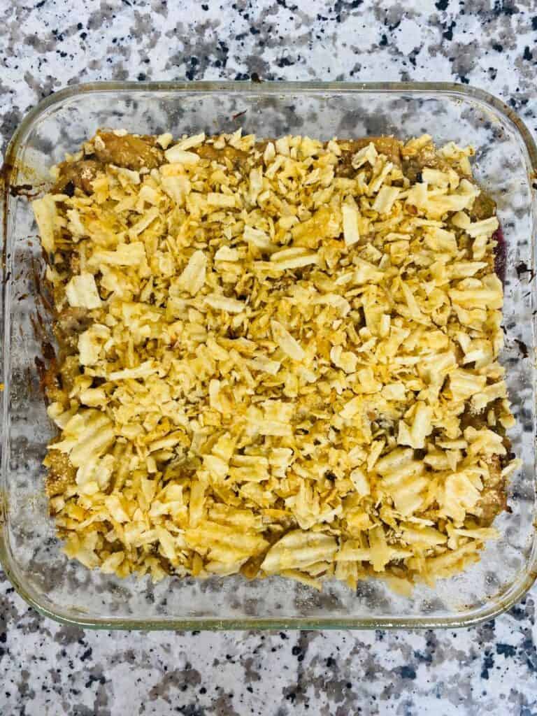 A glass baking dish filled with a casserole topped with a layer of crushed potato chips, sitting on a speckled granite countertop.