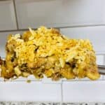 A fork holds a serving of casserole topped with crushed chips, with a tiled backsplash and speckled countertop in the background.