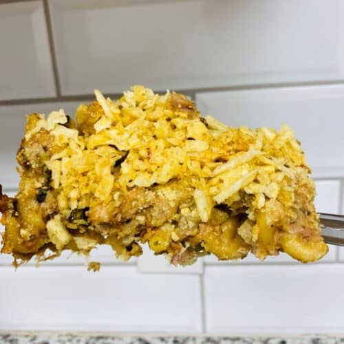 A fork holds a serving of casserole topped with crushed chips, with a tiled backsplash and speckled countertop in the background.