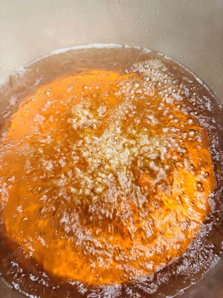 Close-up of hot cider bubbling and frying in a metal pot, with a golden-brown color and visible bubbles rising to the surface.