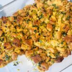 A glass baking dish filled with golden-brown homemade stuffing, featuring toasted bread cubes mixed with herbs and chopped celery.
