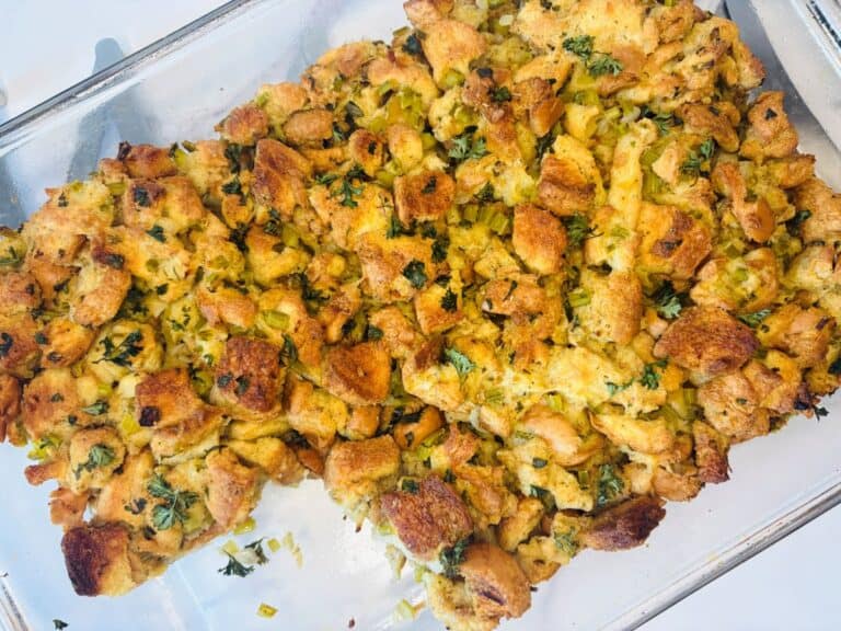 A glass baking dish filled with golden-brown homemade stuffing, featuring toasted bread cubes mixed with herbs and chopped celery.