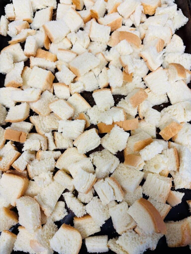 Cubed pieces of white bread spread out in a single layer, likely prepared for making croutons or stuffing. The bread cubes have soft, white centers and light brown crusts visible on some pieces.