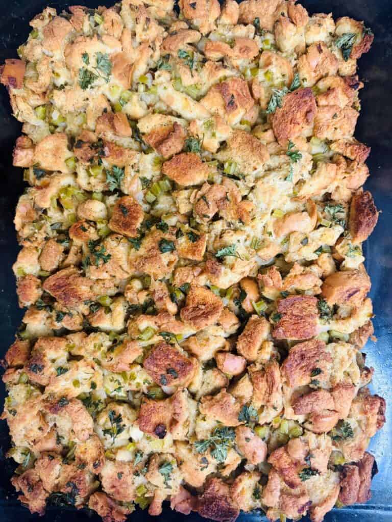 Golden-brown baked stuffing with chunks of bread, herbs, and visible pieces of celery, spread evenly in a rectangular baking dish.