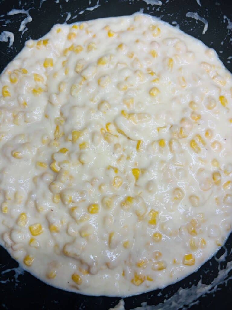 Close-up of creamy corn mixture with visible yellow corn kernels in a thick white sauce, spread out in a pan or shallow dish.