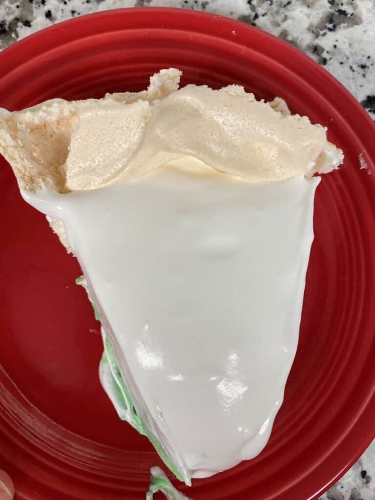 A slice of pie topped with fluffy meringue and white icing, served on a red plate with a granite countertop in the background.
