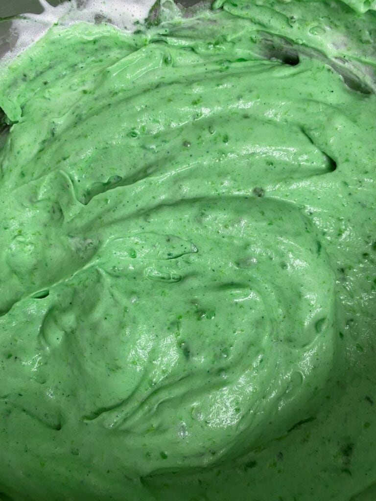 Bright green, creamy mixture with a thick, smooth, and slightly lumpy texture, spread across a surface, possibly a batter or frosting in a mixing bowl.