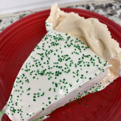 A slice of meringue pie with white topping and green sprinkles sits on a red plate, with a textured crust and creamy filling visible.