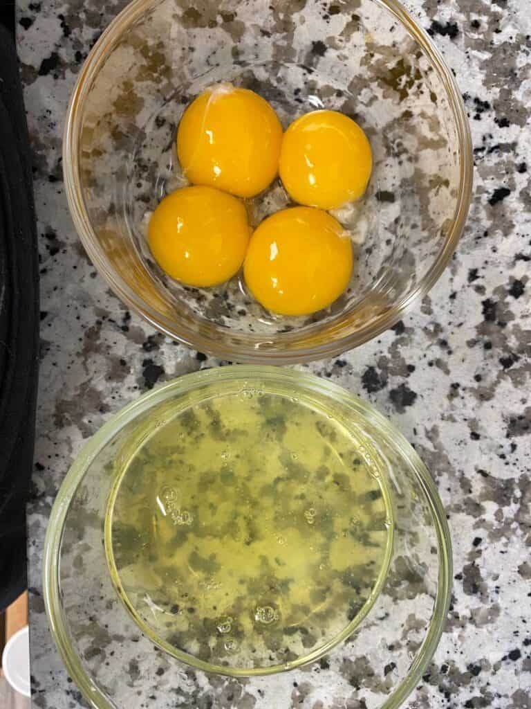 Two glass bowls on a speckled countertop: the top bowl contains four egg yolks, and the bottom bowl contains separated egg whites with a few bubbles.