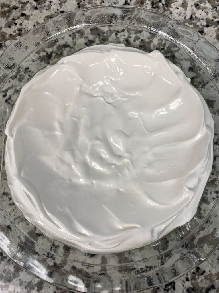 A round glass dish filled with a smooth layer of white whipped topping, resting on a gray and white speckled countertop.