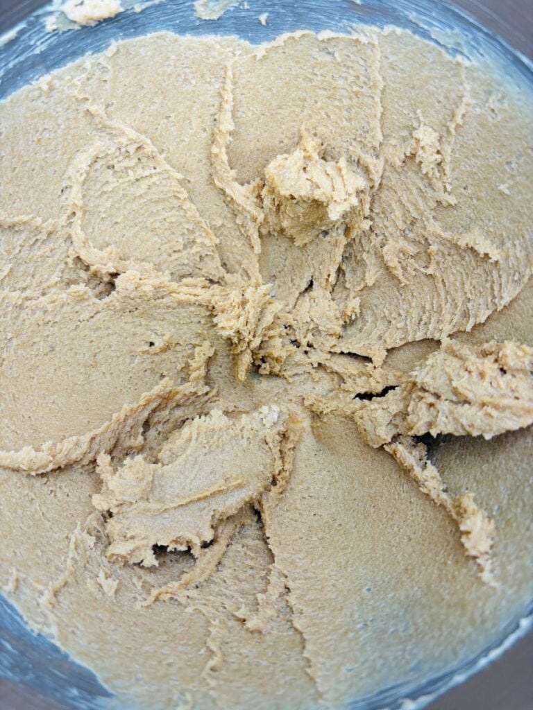 Close-up of creamy, light brown cookie dough spread in a large mixing bowl, showing its smooth and slightly fluffy texture.