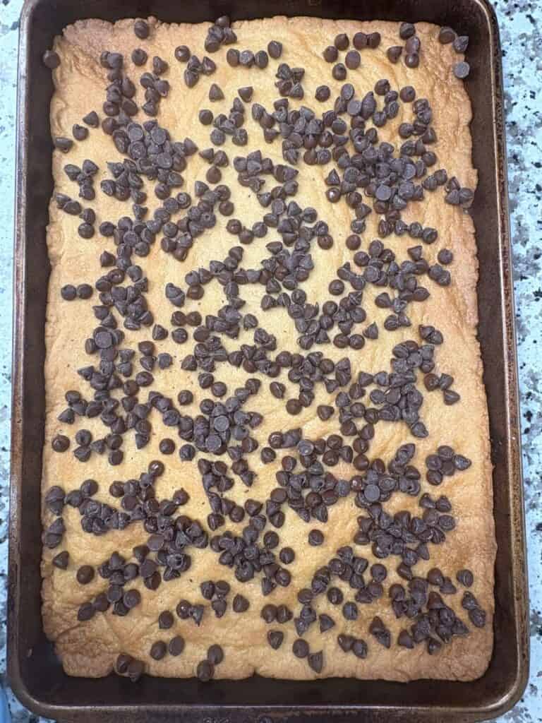 A rectangular pan filled with a large, golden brown cookie topped with scattered chocolate chips sits on a granite countertop.