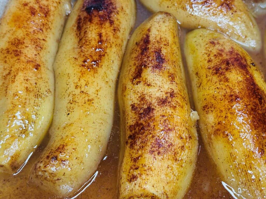 Several peeled bananas cooked in a syrupy sauce and sprinkled with cinnamon.
