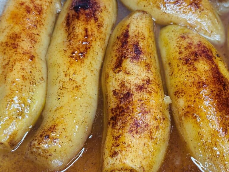 Several peeled bananas cooked in a syrupy sauce and sprinkled with cinnamon.