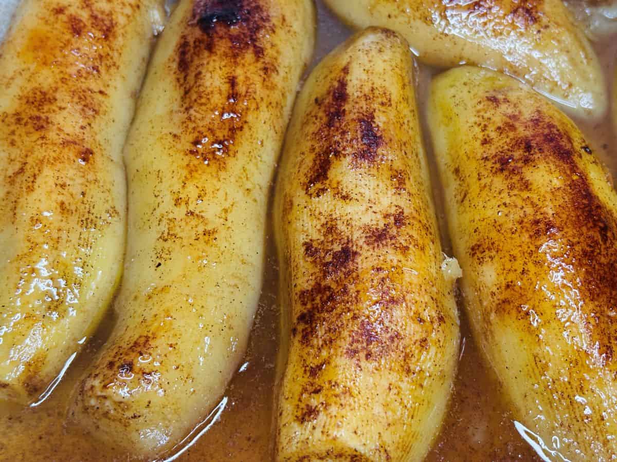 Several peeled bananas cooked in a syrupy sauce and sprinkled with cinnamon.