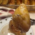 A fork holding a glazed, cooked banana slice above a small plate with creamy sauce.