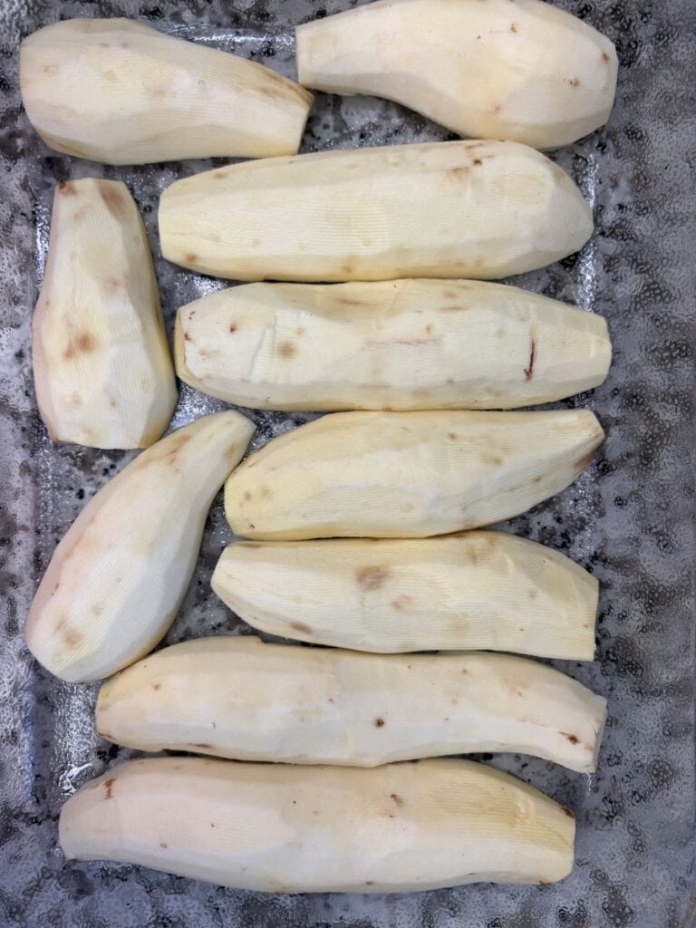 Ten peeled, raw sweet potatoes arranged in a baking dish.