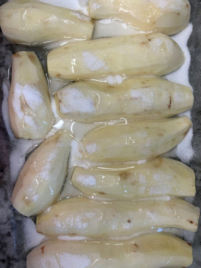 Peeled sweet potatoes in a tray, covered in corn syrup and sprinkled with sugar.