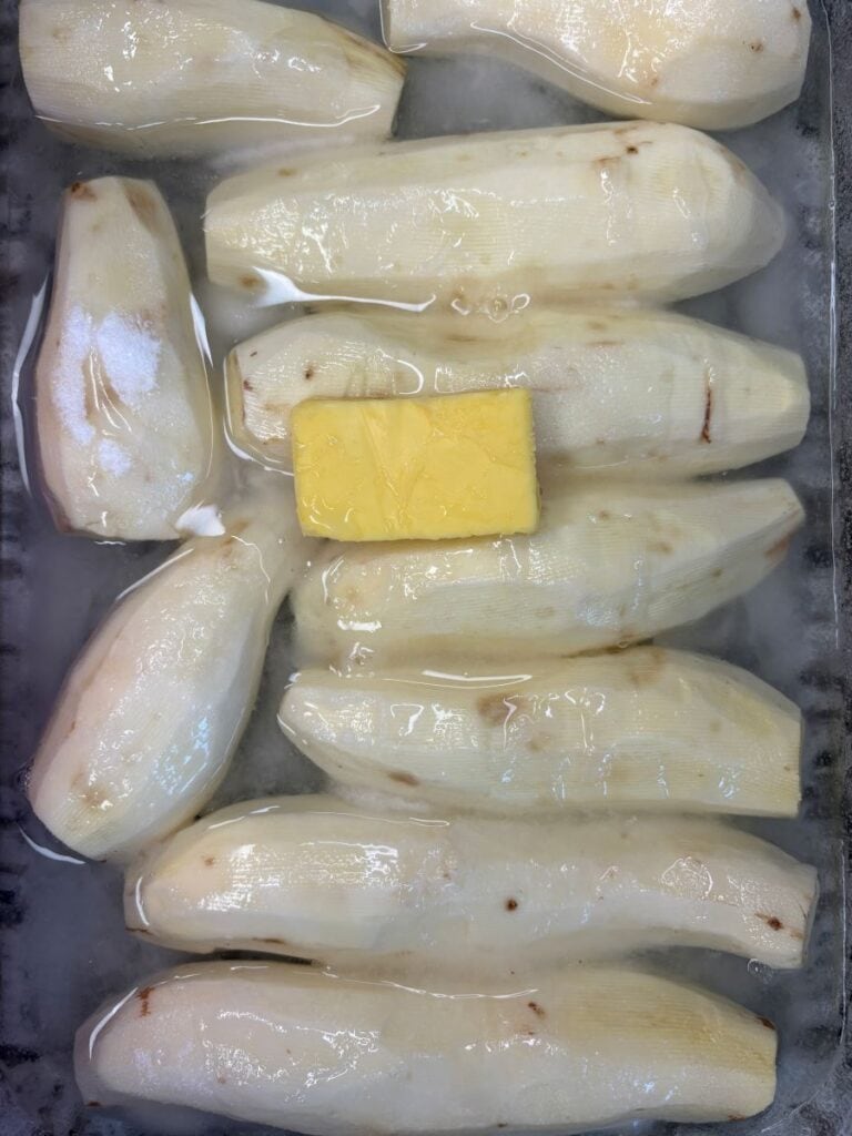 Peeled sweet potatoes soaking in water with a square of butter on top.