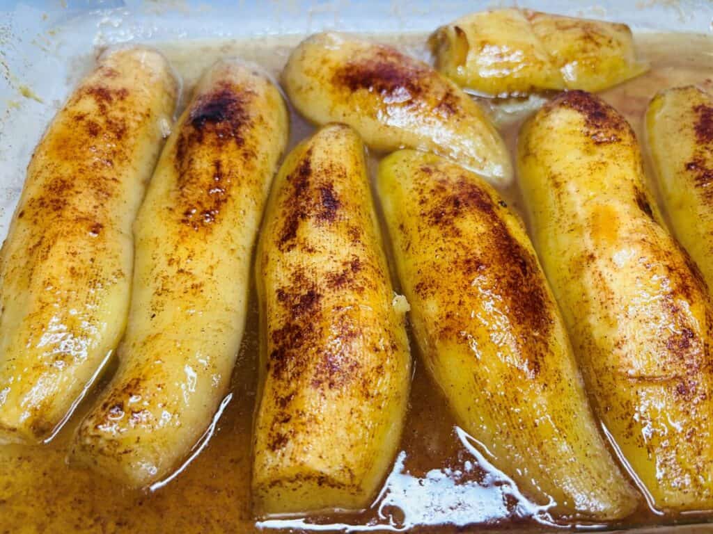 Baked bananas sprinkled with cinnamon in a shallow pool of syrup.