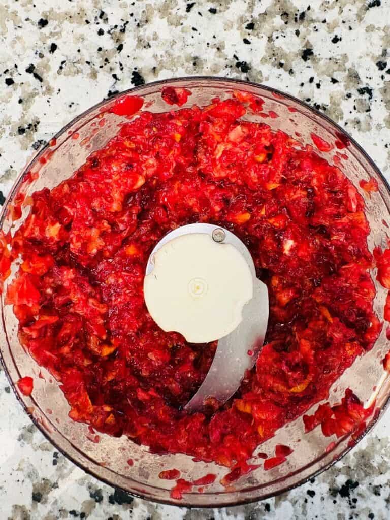 A food processor bowl filled with finely chopped red fruit or vegetables.