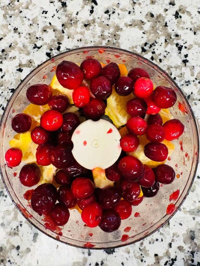A food processor bowl filled with fresh cranberries and orange slices.