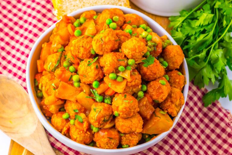 A bowl of Swedish-style meatballs with peas and potato chunks in a savory sauce.