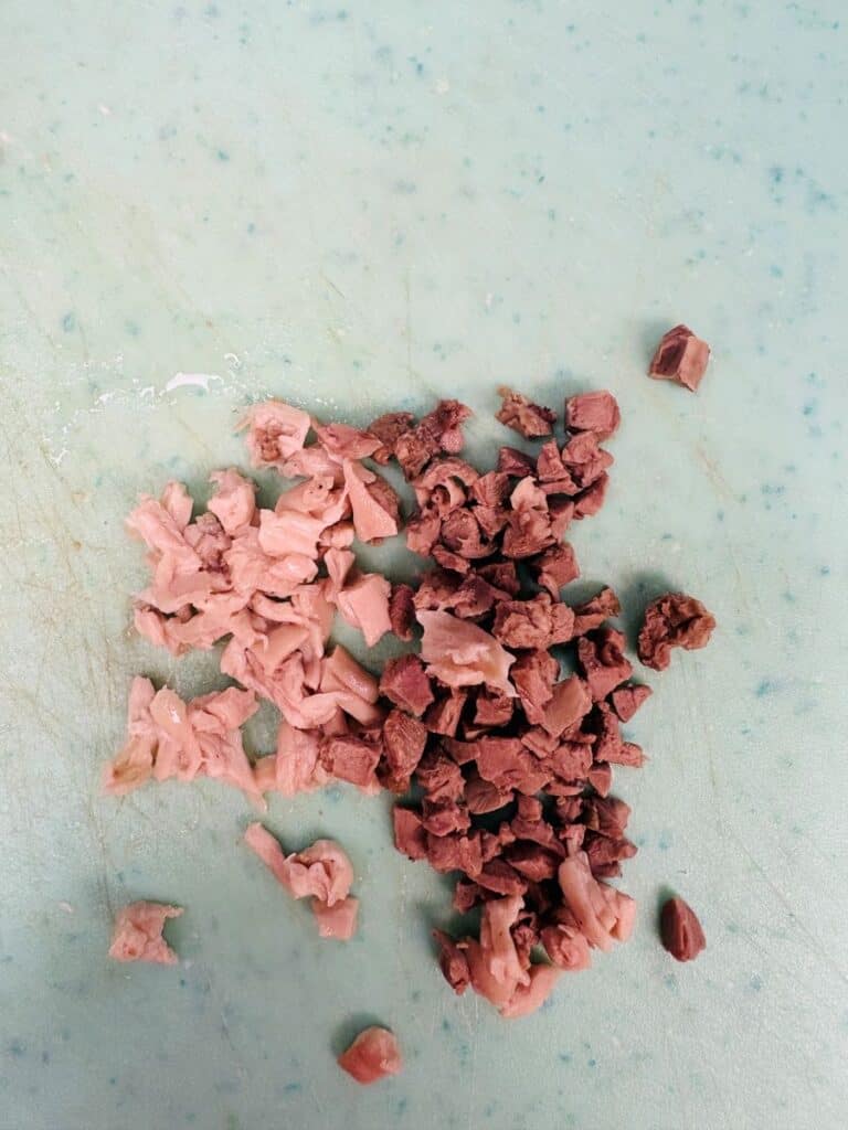 Two small piles of finely chopped meat, one pink and one brown, are arranged on a light green, speckled cutting board.