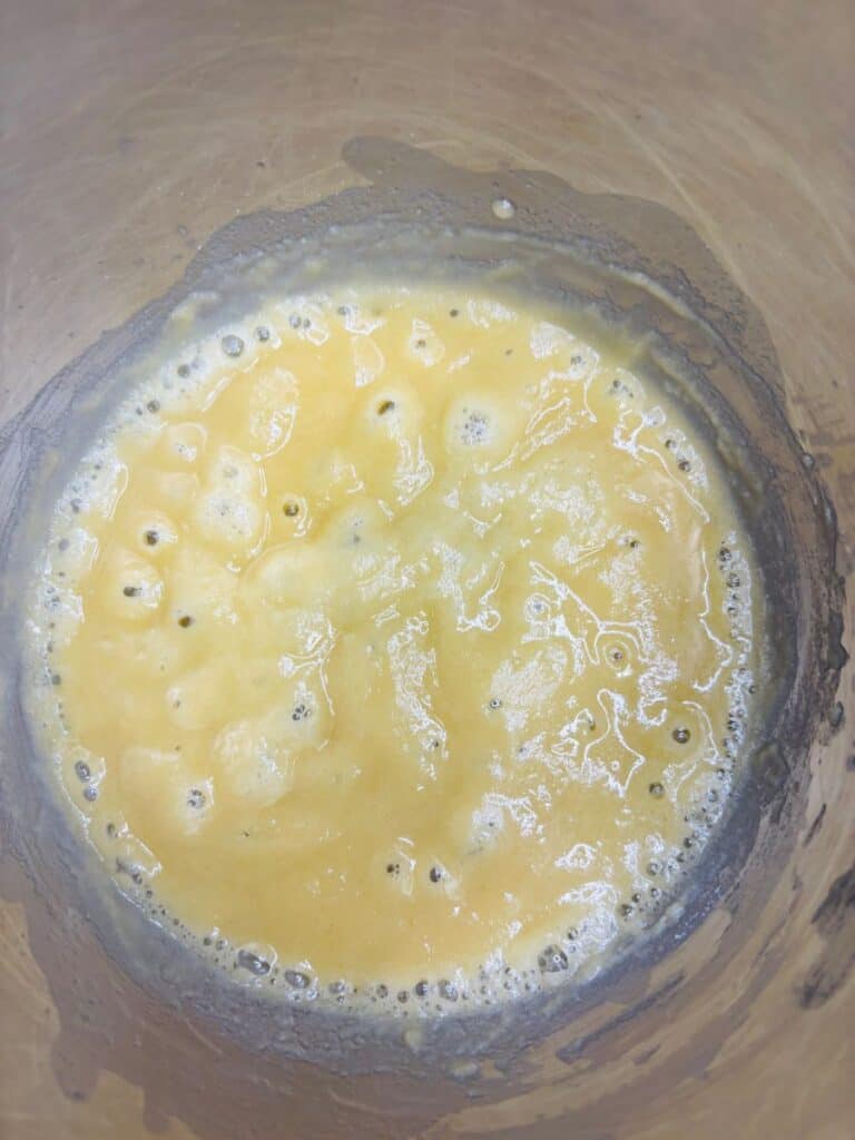 A close-up of a metal mixing bowl containing whisked eggs, showing a yellow, slightly frothy mixture with bubbles on the surface.