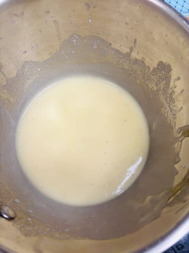A close-up of a pot containing a smooth, pale yellow sauce or mixture, with some residue on the sides of the pot.