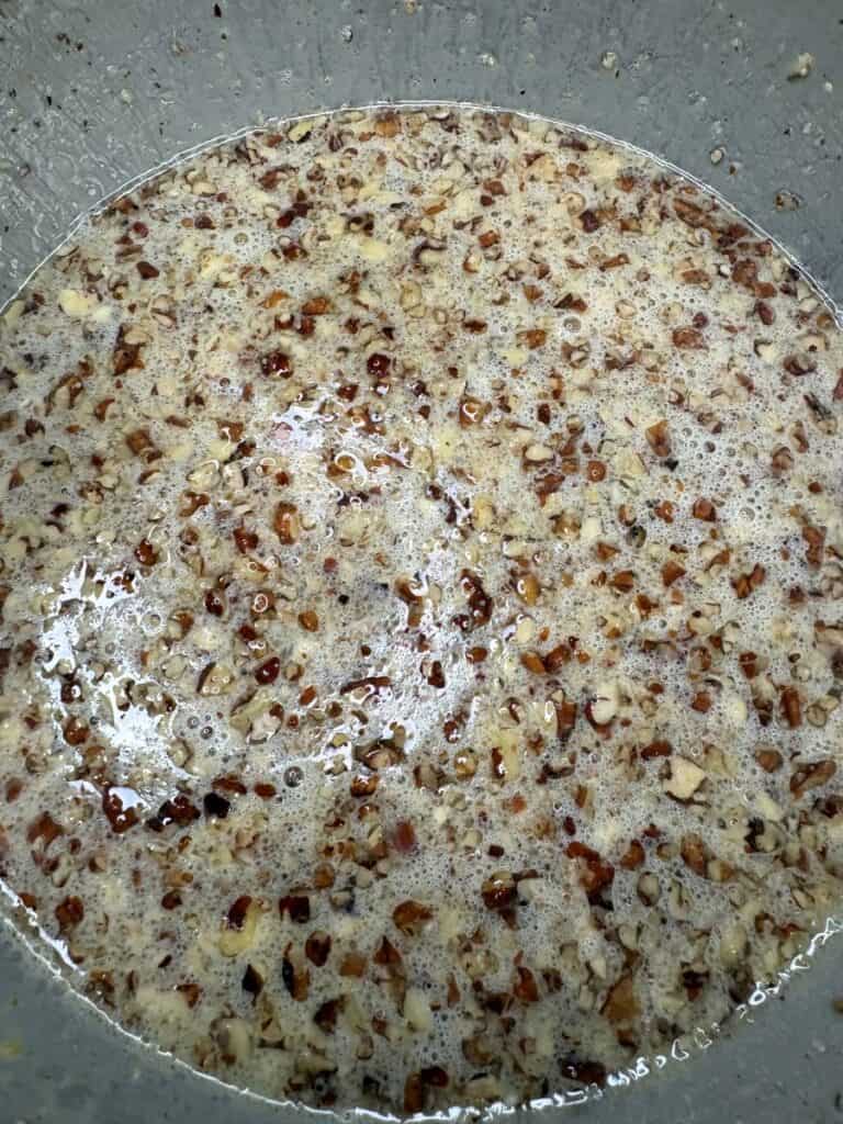 Chopped pecans mixed into a foamy, light-colored liquid inside a metal bowl.