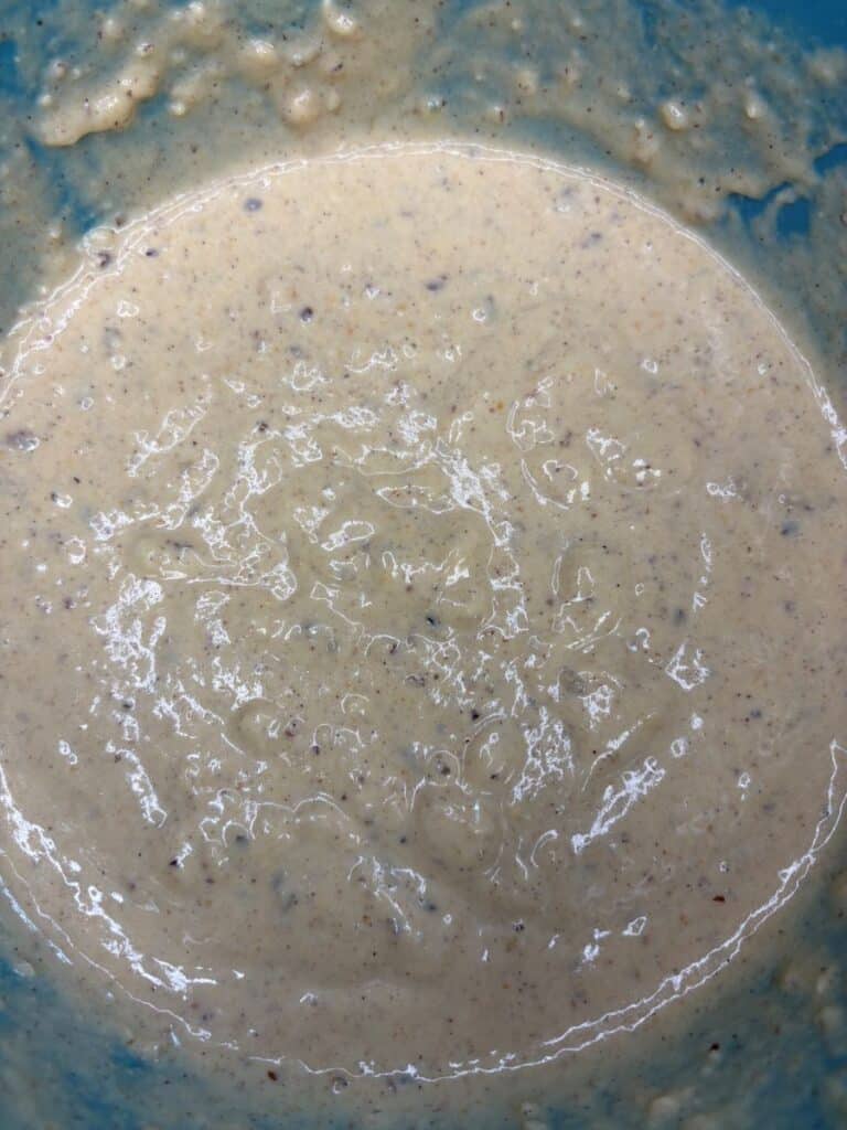 A thick, beige batter with visible dark specks in a blue mixing bowl.