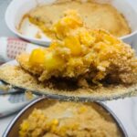 A spoonful of golden corn casserole being lifted from a baking dish.